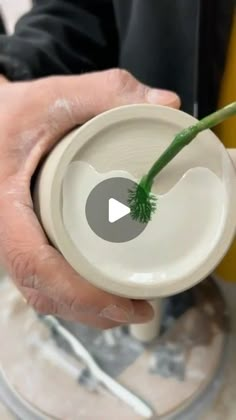 a person holding a small white bowl with a green plant in it's center