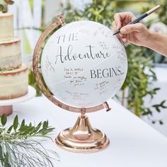 a person writing on a globe at a table with flowers and greenery in the background