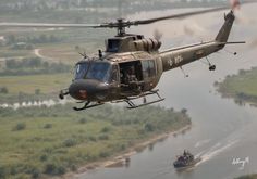 a helicopter flying over a river next to a lush green field