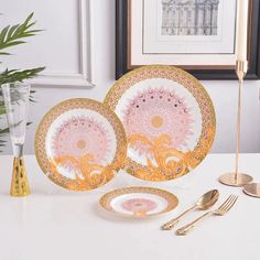 two pink and gold plates sitting on top of a white table next to a vase