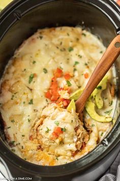 the crock pot is filled with chicken and cheese casserole, topped with a wooden spoon