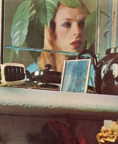 a woman's face is reflected in the mirror behind a shelf with various items on it