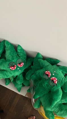 two green stuffed animals sitting next to each other on a wooden floor in front of a white wall