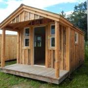 a small wooden building sitting on top of a grass covered field next to a shed