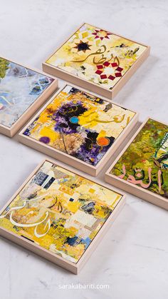 four square paintings are shown on a white counter top, one is yellow and the other is blue