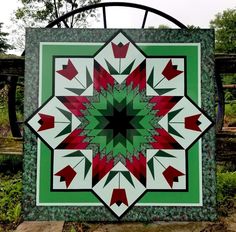 a green and white quilt with red arrows on it in the middle of a garden