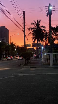 the sun is setting behind palm trees and power lines in an urban area with cars parked on the street