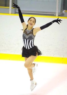 a female figure skating on the ice in a black and white outfit with her arms outstretched