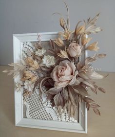 an arrangement of flowers is displayed in a white frame on a wooden table with lace