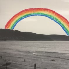 a rainbow colored kite is flying over the ocean with people on the beach below it