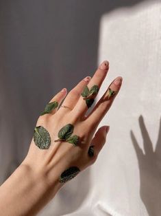 a woman's hand with green leaves painted on it and her fingers in the air