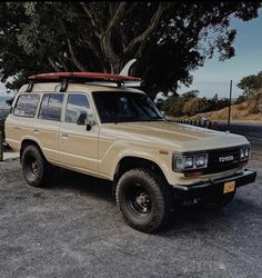 an suv with a surfboard on the roof parked next to a tree