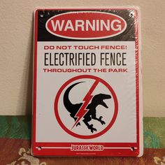 a sign warning people to not touch the electric fence through the park, with an image of a dinosaur on it