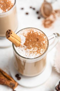 two mugs filled with hot chocolate and cinnamon on a white tablecloth next to cinnamon sticks