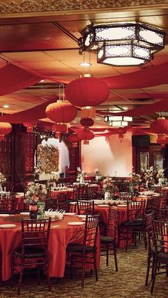 a banquet hall with tables and chairs covered in red tablecloths, lanterns and flowers