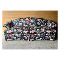 a blue floral couch sitting on top of a wooden floor next to a wall with wood paneling