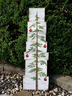 a tall wooden christmas tree sitting on top of a pile of rocks next to a bush