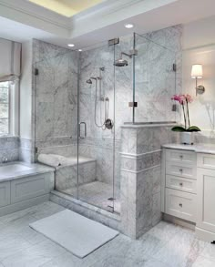 a white bathroom with marble flooring and walls, along with a walk in shower