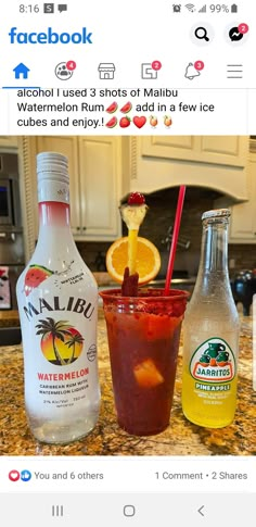 two bottles of alcohol sitting on top of a counter next to a cup filled with fruit