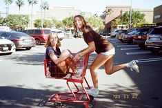 two young women pushing a shopping cart in a parking lot