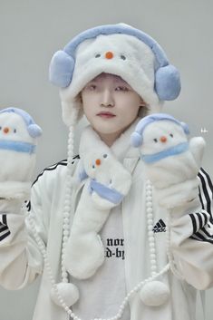 a young man wearing winter clothing and holding two snowman mittens on his hands