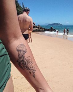 a person with a jellyfish tattoo on their arm at the beach while others walk in the water