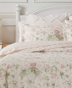 a white bed with pink flowers on it in a bedroom next to a night stand