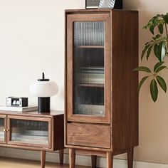 a tall wooden cabinet sitting next to a plant on top of a hard wood floor