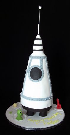 a cake that looks like a space shuttle on top of a black surface with white frosting and blue trimmings