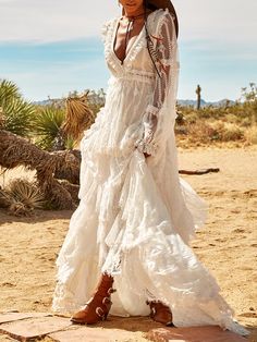 a woman standing in the desert wearing a white dress and cowboy hat with her hands on her hips