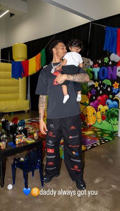 a man holding a baby in his arms while standing next to a table with toys on it