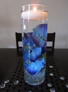 a glass with blue flowers in it sitting on a table next to a lit candle