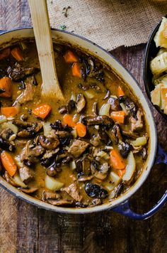 steak and ale soup with mushrooms in a blue pot on a wooden table next to bread