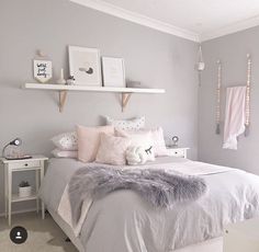 a white and gray bedroom with some pink pillows on the bed, two shelves above the bed