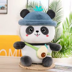 a stuffed panda bear holding a banana on top of a wooden table next to a plant