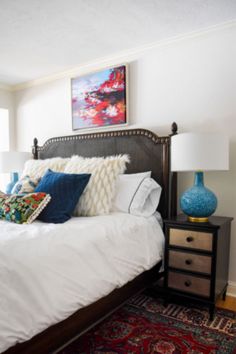 a bed with white sheets and pillows on top of it next to a blue vase