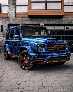 a blue mercedes g - class is parked in front of a brick building with red rims