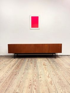 an empty room with wood flooring and a red painting on the wall above it