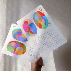 someone is holding up three calendars with circles on them and the numbers are numbered in different colors