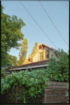 an old house is surrounded by greenery and power lines in the foreground, with a yellow roof