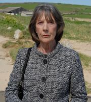 an older woman is standing in front of the ocean with her hands in her pockets