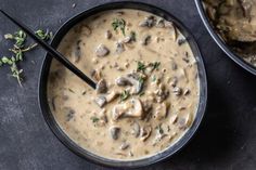 two black bowls filled with mushroom soup on top of a table next to a spoon