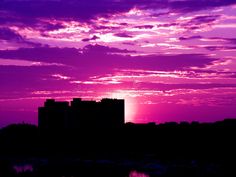 the sun is setting over some buildings in front of a purple and pink sky with clouds