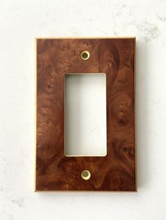 a square wooden frame with two brass screws on the bottom and one white hole in the middle