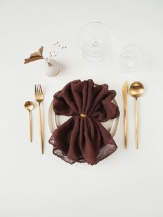 a place setting with napkins, silverware and gold utensils on a white table