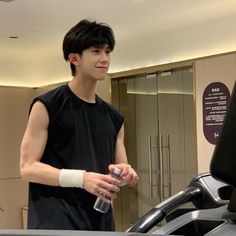 a young man standing in front of a treadmill holding a water bottle and looking at the camera