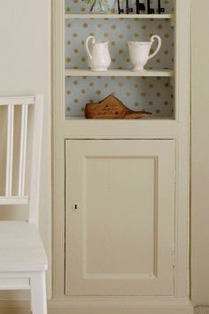 a white chair sitting in front of a book shelf filled with books and vases