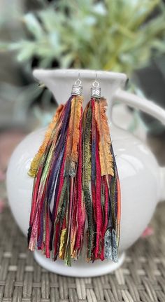 multicolored tassel earrings on white vase with plant in the backgroud