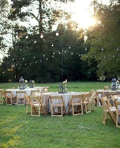 tables and chairs are set up in the grass for an outdoor dinner party with string lights