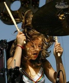 a woman with her hair blowing in the wind while holding a drumstick up to her head